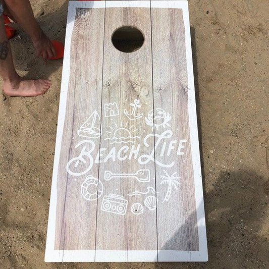 Beach Life themed wood grain cornhole board on a sandy beach.