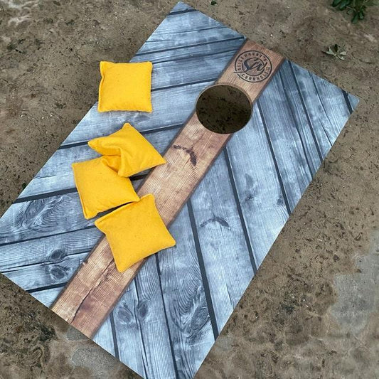 Custom grey wood grain cornhole board with a natural wood stripe and yellow bean bags.