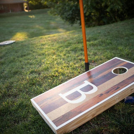 Monogrammed letter B wood grain cornhole board on a backyard lawn