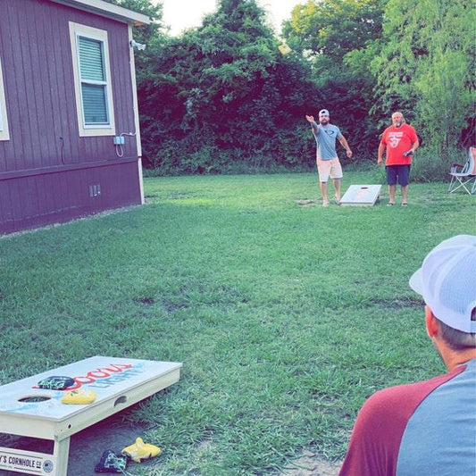People playing cornhole in a grassy yard