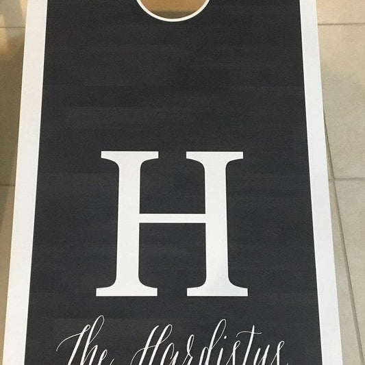  Black cornhole board with white "H" monogram and family name.